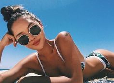 a woman laying on top of a sandy beach next to the ocean wearing sun glasses