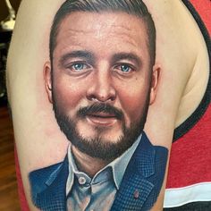 a man with a beard and blue eyes has a portrait tattoo on his arm,