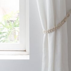 a white curtain with rope hanging from it's side in front of a window