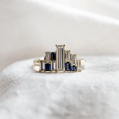 a gold ring with blue and white stones sits on top of a white cloth covered surface