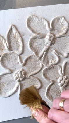 a person using a brush to paint flowers on a piece of paper with gold foil