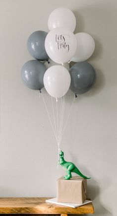 balloons are being released from a box with a toy dinosaur on it, and the balloon is in the shape of a t - rex