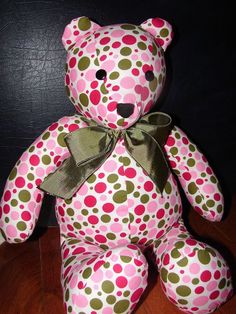 a pink and green polka dot teddy bear sitting on top of a wooden floor next to a black wall