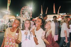 three girls are eating ice cream at an amusement park with ferris wheel in the background