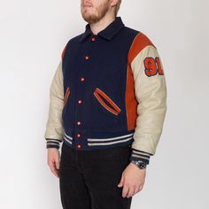 Vintage 70s letterman jacket from a high school team called the Terrors, in navy blue wool with off-white leather sleeves, orange color blocking, and striped knit trim. Lightly distressed. Measurements and Condition: Fits like: Labeled size 50, fits modern men's XL Fabric: Feels like a wool shell, leather sleeves, acrylic knit trim, and quilted nylon lining with polyester fill Brand: Ripon Jackets, made in USA Condition: Lightly distressed, with light general wear, some spots and discoloration on the sleeves, faint discoloration on the cuffs and middle of the patch on the back, and a few other minor scattered small faint spots. Length: 25.5" Chest: 52" Waist: 40" to 44" Shoulders (seam to seam): 23" Sleeve: 24" Shown on a 6'4" model, who usually wears a size extra large. See our FAQ for mo Collegiate Varsity Jacket With Pockets For Fall, Collegiate Fall Varsity Jacket With Pockets, Collegiate Blue Outerwear For Game Day, Retro Long Sleeve Varsity Jacket For Sports, Blue Varsity Jacket With Baseball Collar For School, Retro Outerwear With Baseball Collar And Pockets, Blue Outerwear With Baseball Collar For School, Varsity Sport Coat With Pockets For Fall, Fitted Varsity Jacket With Pockets