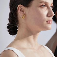 a woman in white shirt and gold earrings looking off to the side