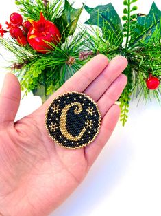 a hand holding a small beaded brooch with the letter c on it's side