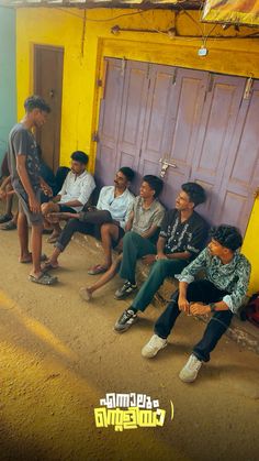 a group of young men sitting next to each other in front of a yellow building