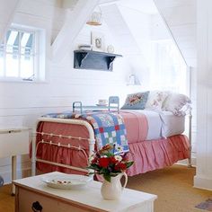 a bed room with a neatly made bed next to a dresser and table in front of it