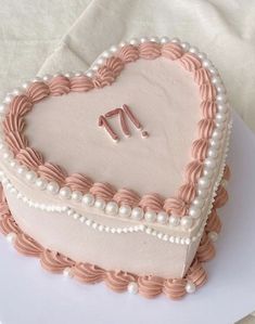 a heart shaped cake decorated with pearls and pink icing on a white tablecloth