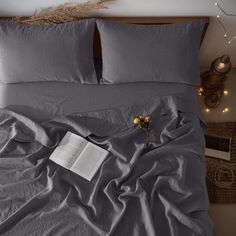 an open book is laying on a bed with grey sheets and pillows, surrounded by string lights