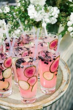 several glasses filled with drinks sitting on top of a wooden tray next to flowers and greenery