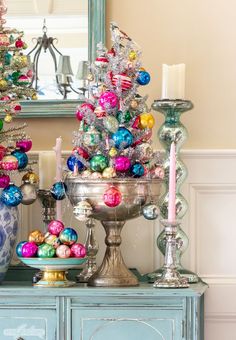 a christmas tree is decorated with ornaments and candles on a table in front of a mirror