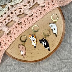 four key chains with cats on them sitting on top of a piece of wood next to a crochet blanket