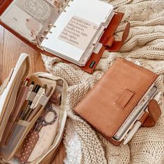 the contents of a purse sitting on top of a wooden floor next to an open notebook