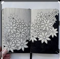 a hand holding an open notebook with flowers drawn on the pages and in front of it