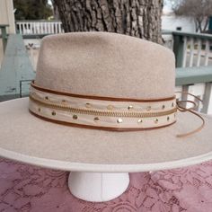 We love what can be done with any type of materials our design team finds. Take a look at this zipper and gold tile hatband. The band is 22.5" x 1.5" and has adjustable tan ties in the back so it can fit hats from 22.5-34". The bottom layer is a soft sorrel brown leather that has been topped with a tan and gold zipper. The zipper runs the entire length of the hatband and really compliments the gold swarvokski tiles that have been added. Something you can wear on your hat every day and we know pe Luxury Adjustable Brown Hat Bands, Adjustable Gold Hats For Fall, Adjustable Gold Hat For Fall, Gold Flat Brim Hat Bands For Spring, Trendy Adjustable Gold Hats, Adjustable Hat Bands For Fall Festival, Luxury Hat Bands For Western-themed Events With Curved Brim, Brown Hat Bands For Winter, One Size Fits Most, Adjustable Gold Hats For Festivals