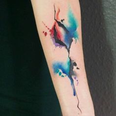 a woman's arm with a colorful watercolor tattoo design on the left forearm