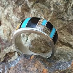 This beautiful Sterling Silver Ring, as part of the Turquoise Creek Collection, features Black Jade, Picture Jasper, and Kingman Turquoise. Dimensions: Ring Width 7/16"; Ring Shank 3/16" The ring is designed by David Rosales, one of the finest contemporary Southwest Artists in the world. He is the founder and co-owner of Supersmiths, Inc. of Gallup, NM. Each ring is custom made and carries a lifetime guarantee. Multicolor Inlay Rings For Anniversary, Artisan Rings With Inlay For Anniversary, Anniversary Multicolor Inlay Rings, Unique Blue Turquoise Ring With Inlay, Blue Turquoise Ring With Inlay, Southwestern Style Rings With Inlay, Turquoise Inlay Round Rings, Southwestern Round Rings With Inlay, Turquoise Inlay Rings As A Gift