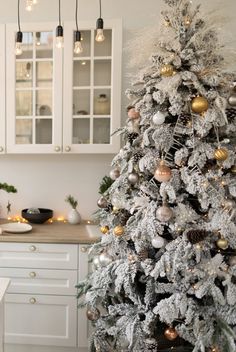 a white christmas tree with gold and silver ornaments is in the corner of this kitchen