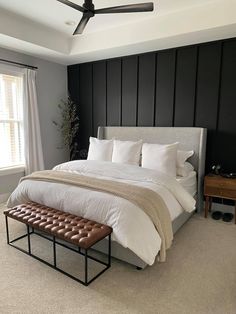 a bedroom with a large bed, white sheets and brown leather foot stools in front of the window