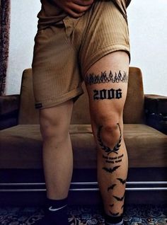 a man with tattoos on his legs standing in front of a couch