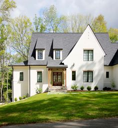 a large white house with black roof and two story windows on the front of it