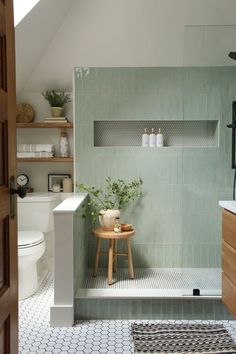 a white toilet sitting next to a walk in shower under a bathroom window with green tiles