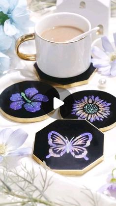 four coasters with purple flowers and a cup of coffee on the table next to them