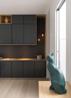 a cat statue sitting on top of a wooden floor next to a kitchen counter and cabinets