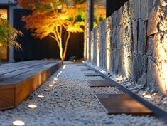 a stone wall next to a walkway with trees in the background and lights shining down on it