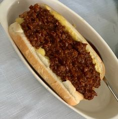 a chili dog in a white dish with a fork on the side, ready to be eaten