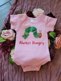 "This baby bodysuit is inspired by the book A Very Hungry Caterpillar written by Eric Carle. You can personalize the words at no extra charge. This is a great shirt to be personalized for a 1st birthday party.  The shirt will say \"Always Hungry\" unless personalization is requested. The product is 100% cotton and very comfortable. The fabric is completely opaque and are machine washable." Cute Fitted Bodysuit With Cartoon Print, Playful Fitted Onesie For Birthday, Customizable Fitted Onesie For First Birthday, Fitted Onesie With Cartoon Print For Spring, Fitted Short Sleeve Onesie For Birthday, Fitted Short Sleeve Fun Bodysuit, Fun Fitted Short Sleeve Bodysuit, Fitted Short Sleeve Bodysuit With Cartoon Print, Fitted Pink Bodysuit With Cartoon Print