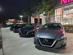 several cars are parked in front of a nissan dealership at night with palm trees