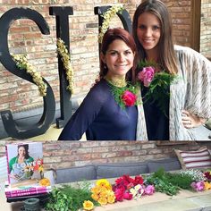 two women standing next to each other in front of a sign with flowers on it