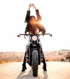 a woman sitting on the back of a motorcycle with her hands up in the air