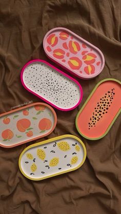 four trays with different designs on them sitting on a bed together, one is empty and the other has fruit print