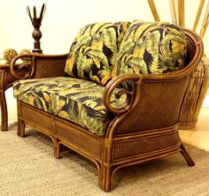 a wicker couch with tropical print upholstered on the armrests next to a side table