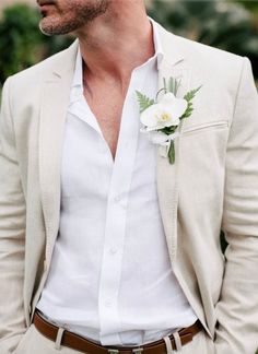 a man wearing a white suit and flower boutonniere is looking to his left