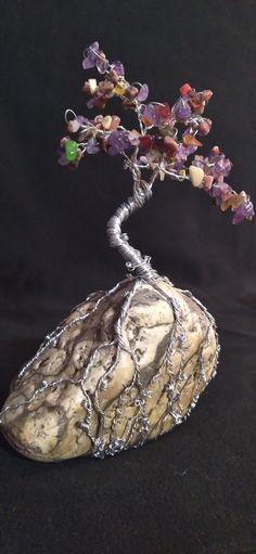 a wire tree on top of a rock with purple and green beads hanging from it