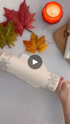 a person holding a roll of paper next to autumn leaves and candles on a table