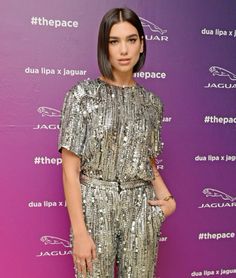 a woman standing in front of a purple wall wearing silver sequin jumpsuits