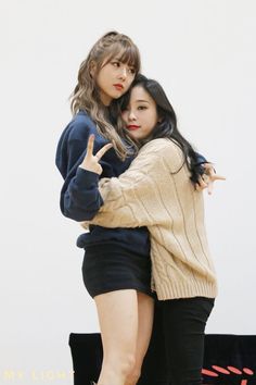 two young women standing next to each other with their arms around one another and making the peace sign