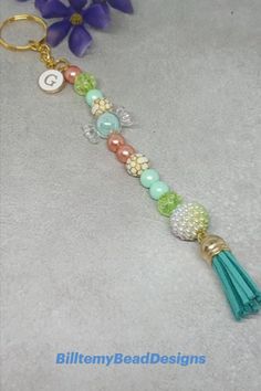 a keychain with beads and tassels on it next to purple flowers