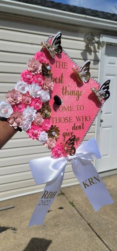 someone holding up a pink and white graduation cap with butterflies on the front, in front of a garage door