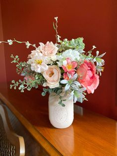 a vase filled with lots of flowers on top of a wooden table next to a red wall