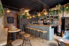 a bar with wooden stools and plants hanging from the ceiling in a brick walled room