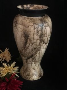 a marbled vase sitting next to flowers on a black background with space for text