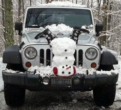 a white teddy bear sitting on the hood of a jeep with snow piled all over it