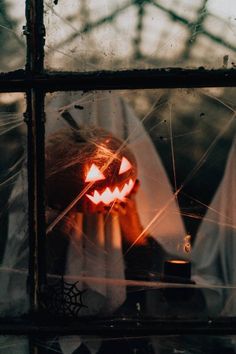 a scary pumpkin carved into the side of a window with spider webs around it